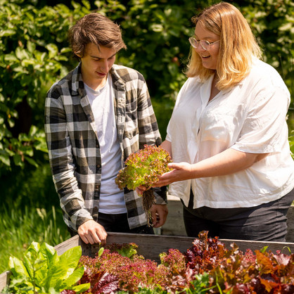 Two young people standing in front of a raised bed with lettuce and holding a picked head of lettuce in their hands