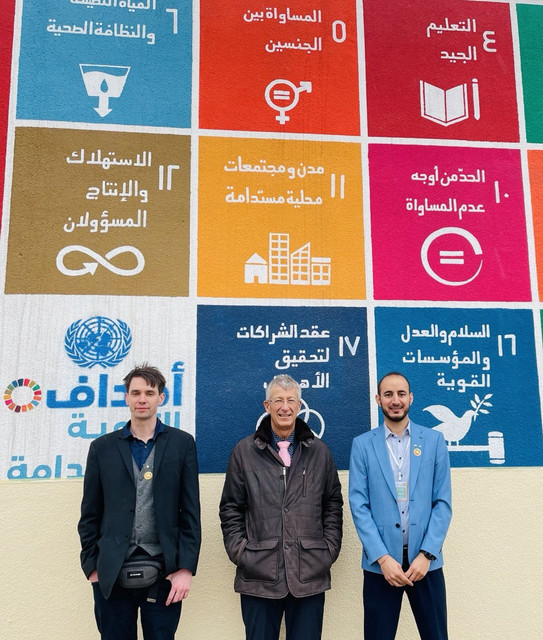 Studierende Universität Mossul Drei Studierende stehen vor einem Plakat der Universität Mossul.