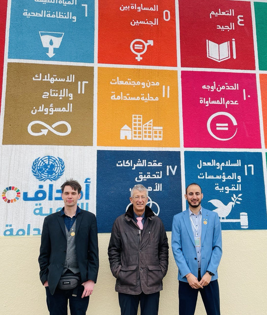 Studierende Universität Mossul Drei Studierende stehen vor einem Plakat der Universität Mossul.