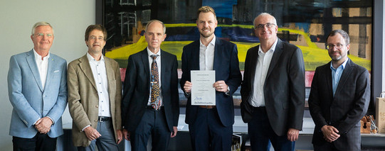 Das Foto zeigt Prof. Peitz mit fünf anderen Personen der Hochschule bei seiner Neuberufung. Im Hintergrund befindet sich ein großes buntes Kunstwerk.