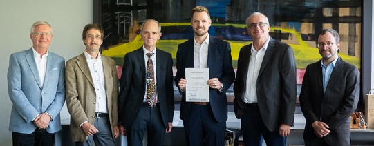 Das Foto zeigt Prof. Peitz mit fünf anderen Personen der Hochschule bei seiner Neuberufung. Im Hintergrund befindet sich ein großes buntes Kunstwerk.