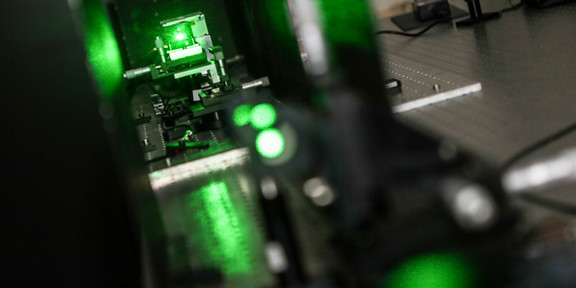 Experimentelle Physik Nahaufnahme einer metallischen Maschine, die grün leuchtet.