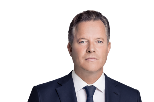 Ein Portraitfoto von einem Mann in einem schwarzen Anzug mit Krawatte.