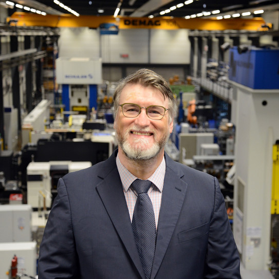 Yannis P. Korkolis Portrait eines lächelnden Manns im Anzug, der in einer Experimentierhalle steht