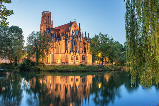 Eine beleuchtete christliche Kirche bei Dämmerung an einem See. 