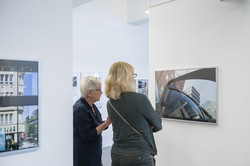 Zwei Frauen stehen zwischen zwei Ausstellungswänden. Sie unterhalten sich über eine Fotografie, die die Spiegelung in einer Autotür zeigt.