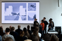 Several people present architectural designs to a seated audience.