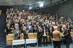 Das Publikum im Audimax applaudiert stehend, während Frances Arnold Blumen überreicht bekommt.