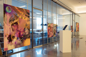 Mehrere Gemälde sind an der Glasfront eines Seminarraumes ausgestellt.