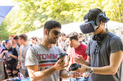 Ein Mann probiert eine VR-Brille aus, ein anderer Mann hilft ihm dabei