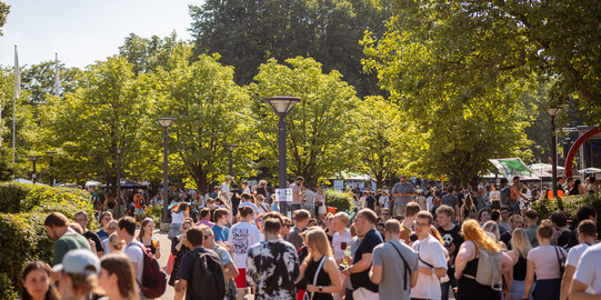 Besucher*innen eines Sommerfests sind auf einem Uni-Campus.