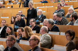 Mehrere Personen sitzen in einem Hörsaal, eine Person hält ein Mikrophon in der Hand.