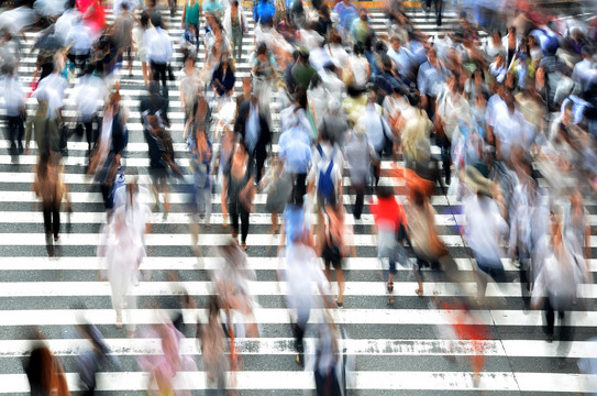 The photo shows blurred many passers-by walking across a crosswalk.