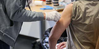 Eine Person trägt Gummihandschuhe und desinfiziert den nackten Oberarm einer anderen Person.