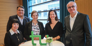 Gruppenfoto mit fünf Personen. Auf dem Stehtisch vor ihnen steht ein TU-Logo