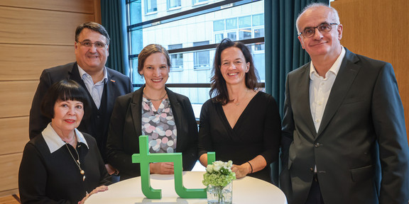 Gruppenfoto mit fünf Personen. Auf dem Stehtisch vor ihnen steht ein TU-Logo
