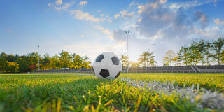 Foto: Ein Fußball liegt auf einem Fußballfeld. Hinter dem Ball scheint die Sonne hervor.