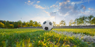 Foto: Ein Fußball liegt auf einem Fußballfeld. Hinter dem Ball scheint die Sonne hervor.