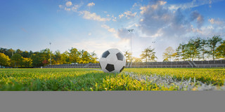 Foto: Ein Fußball liegt auf einem Fußballfeld. Hinter dem Ball scheint die Sonne hervor.