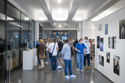 Mehrere Personen schauen sich Bilder an einer weißen Wand einer Kunstausstellung an.