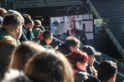 Die neuen Studierenden schauen auf die Video-Leinwand im Stadion, auf dem Ursula Gathers Videogruß zu sehen ist. 