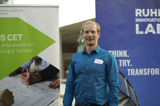 Foto: Eine Person steht zwischen zwei Roll‑up‑Bannern bei einer Veranstaltung.
