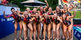 Gruppenfoto: Spielerinnen jubeln im Badeanzug am Beckenrand, im Hintergrund Zuschauer auf der Tribüne.