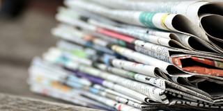 A stack of newspapers on a wooden table.