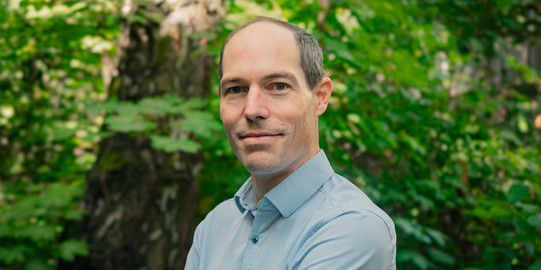 Porträtfoto von Prof. Armin Lühr: Prof. Lühr trägt ein hellblaues Hemd und steht in einem grünen Wald.