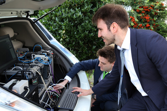Zwei Männer schauen sich die Rechnertechnik im Kofferraum eines Autos an.