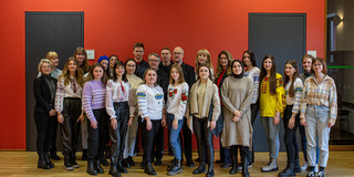 Several people are standing in front of a red wall.