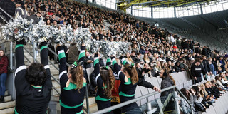 Ersti-Begrüßung 2024 Eine Stadiontribüne voller junger Menschen, unten stehen Cheerleader in schwarz-grünen Kostümen und silbernen Pompons.