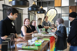 Studierende stehen an einem Infostand mit Flyern und Postern. Vor dem Stand stehen eine Frau und ein Mann, die sich die Flyer angucken.