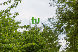 August TU-Logo auf dem Mathetower, im Vordergrund Blattwerk
