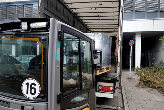 Auf dem Foto sieht man, wie ein kleiner Gabelstapler den LKW belädt.