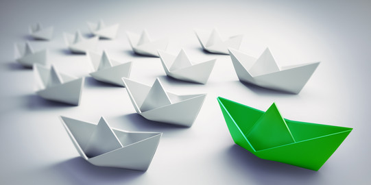Paper boat fleet on white background, green boat sails ahead