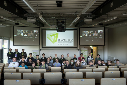 Menschen sind für ein Gruppenfoto in einem Hörsaal vor Leinwänden versammelt.