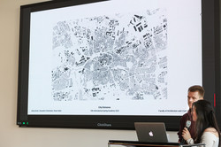 Spring Academy A woman and a man present a floor plan of the city of Dortmund in front of a group of people.