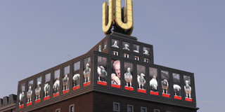 A tall building with a glowing U on the roof against an evening sky.