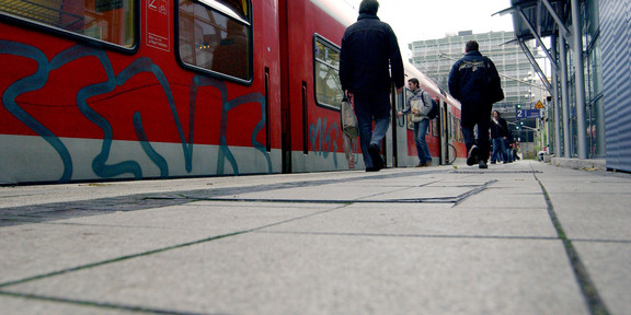 Zug hält am Bahnsteig, Passanten steigen aus