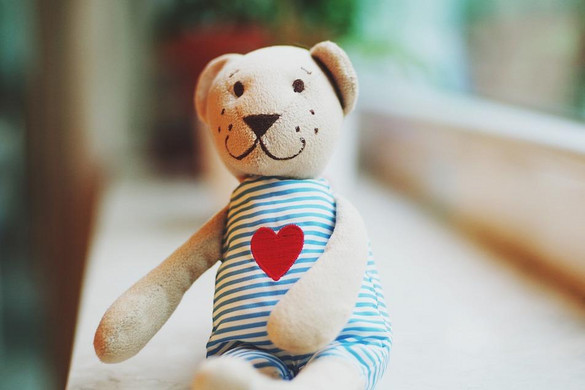 Teddy mit gestreiftem Kleid und rotem Herz auf dem Bauch