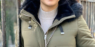 A woman smiles at the camera. She is standing in front of a fence.