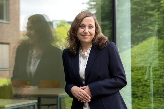 Portrait of Prof. Nadja Dörflinger: Prof. Dörflinger is wearing a dark blazer and leaning against a glass facade.