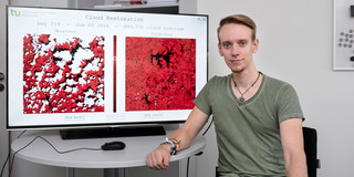 Raphael Fischer Foto von Raphael Fischer. Er sitzt vor einem Bildschirm, der zwei Satellitenbilder zeigt.