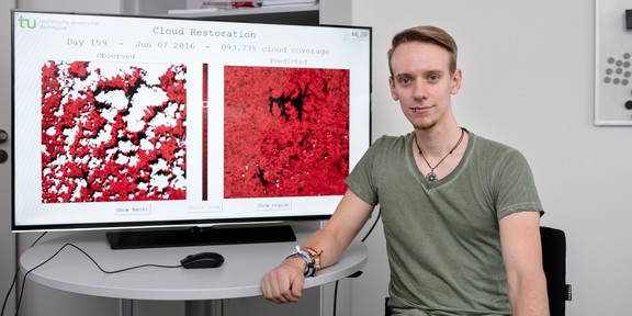 Photo of Raphael Fischer. He is sitting in front of a screen showing two satellite images.