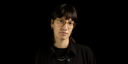 Porträtfoto von Prof. Magdalena Zabek: Porf. Zabek trägt eine Brille und dunkle Kleidung. Sie steht vor einem schwarzen Hintergrund.