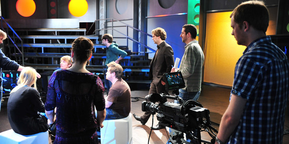 People sit in the studio. a man watches the action through a camera