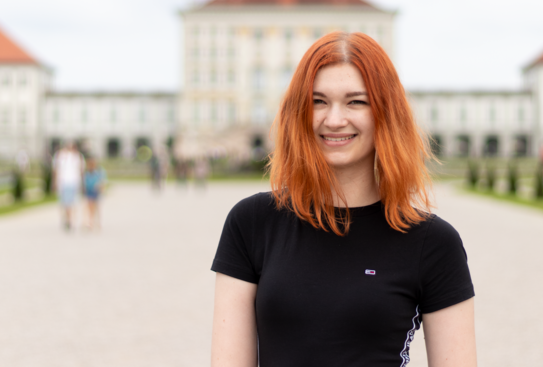 Eine Frau mit roten Haaren und schwarzen T-Shirt lächelt in die Kamera.