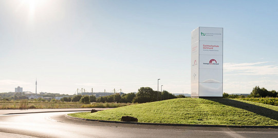 A roundabout with a sign that includes the logos of TU Dortmund University and the University of Applied Sciences and Arts of Dortmund.