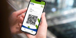Zwei Hände halten ein Smartphone, dessen Bildschirm einen QR-Code anzeigt